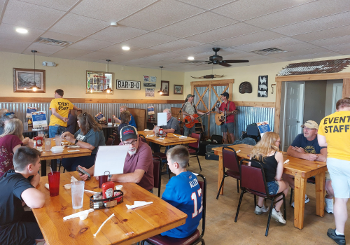 Optimist Club members eating at the fish fry while the musician plays music in the background